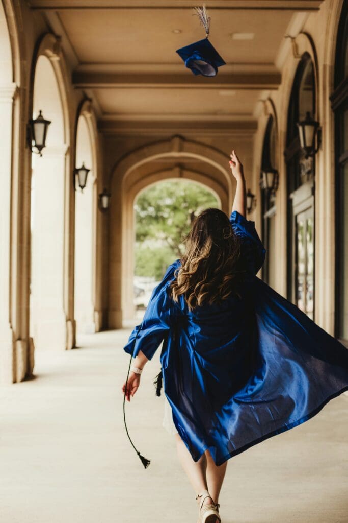Woman throwing graduation hat in halls of academia (view from back)